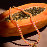 Necklace with a fish charm draped over a halved papaya on a dark background