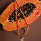 Peach-colored fruit with a beaded necklace draped over it on a brown background