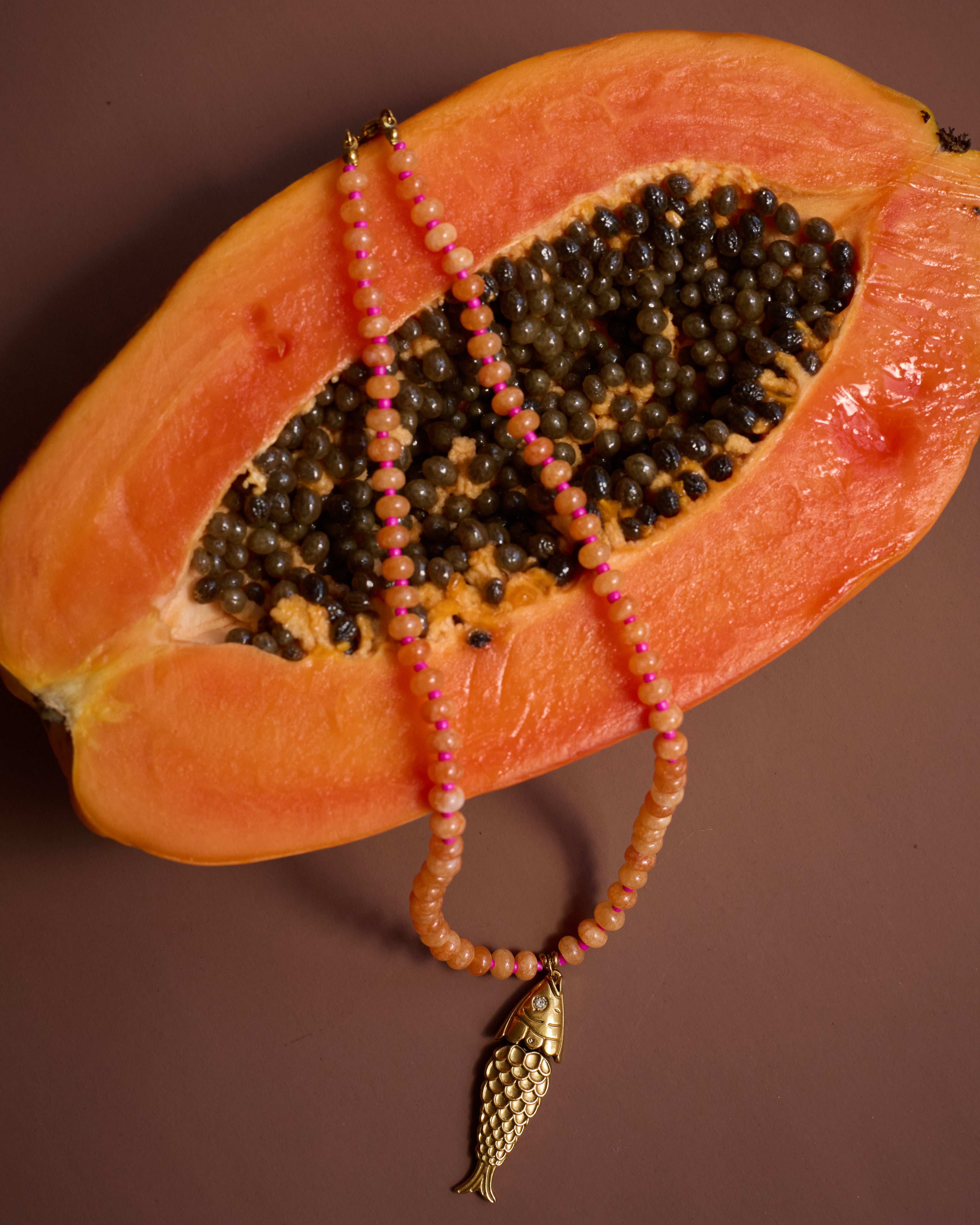 Peach-colored fruit with a beaded necklace draped over it on a brown background