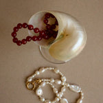 Red beaded necklace and white pearl necklace on a beige surface