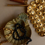 Gold necklace with black beads and decorative elements on a beige background