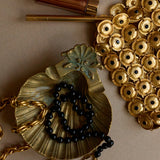 Gold necklace with black beads and decorative elements on a beige background