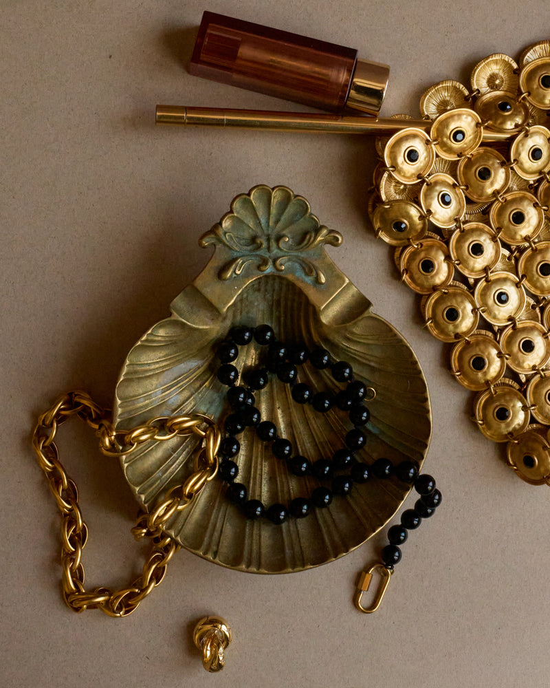 Decorative object with black beads and gold chain on a beige background