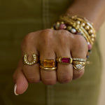 Close-up of a hand wearing multiple gold rings with gemstones against a blurred background.