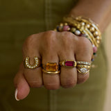 Close-up of a hand wearing multiple gold rings with gemstones against a blurred background.