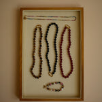 Jewelry display with necklaces in a wooden frame on a beige wall.