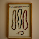 Jewelry display with necklaces in a wooden frame on a beige wall.