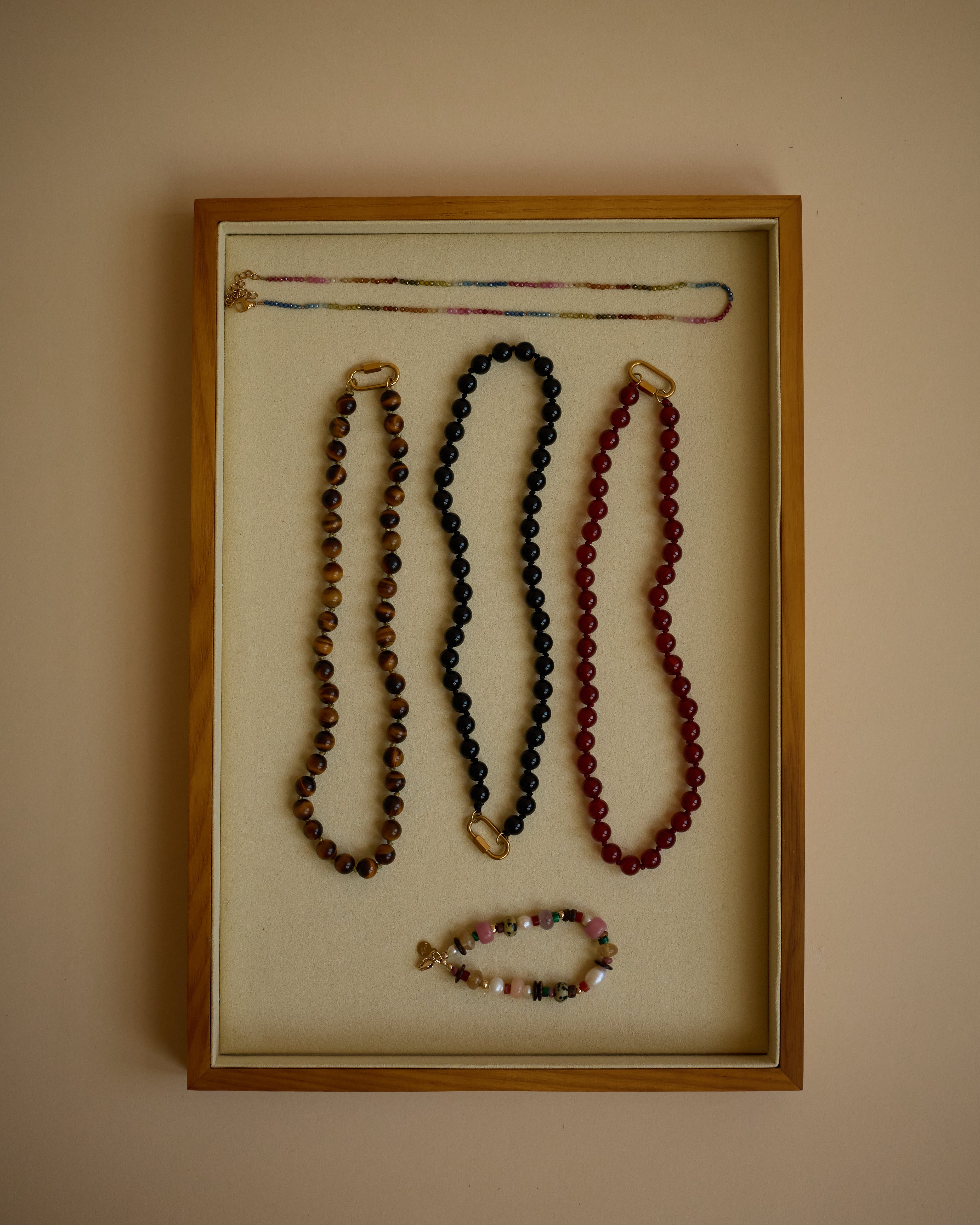 Jewelry display with necklaces in a wooden frame on a beige wall.