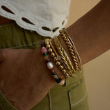 Close-up of a wrist wearing gold bracelets with colorful beads against a neutral background