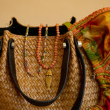 Woven handbag with colorful beads and a fish charm on a beige background