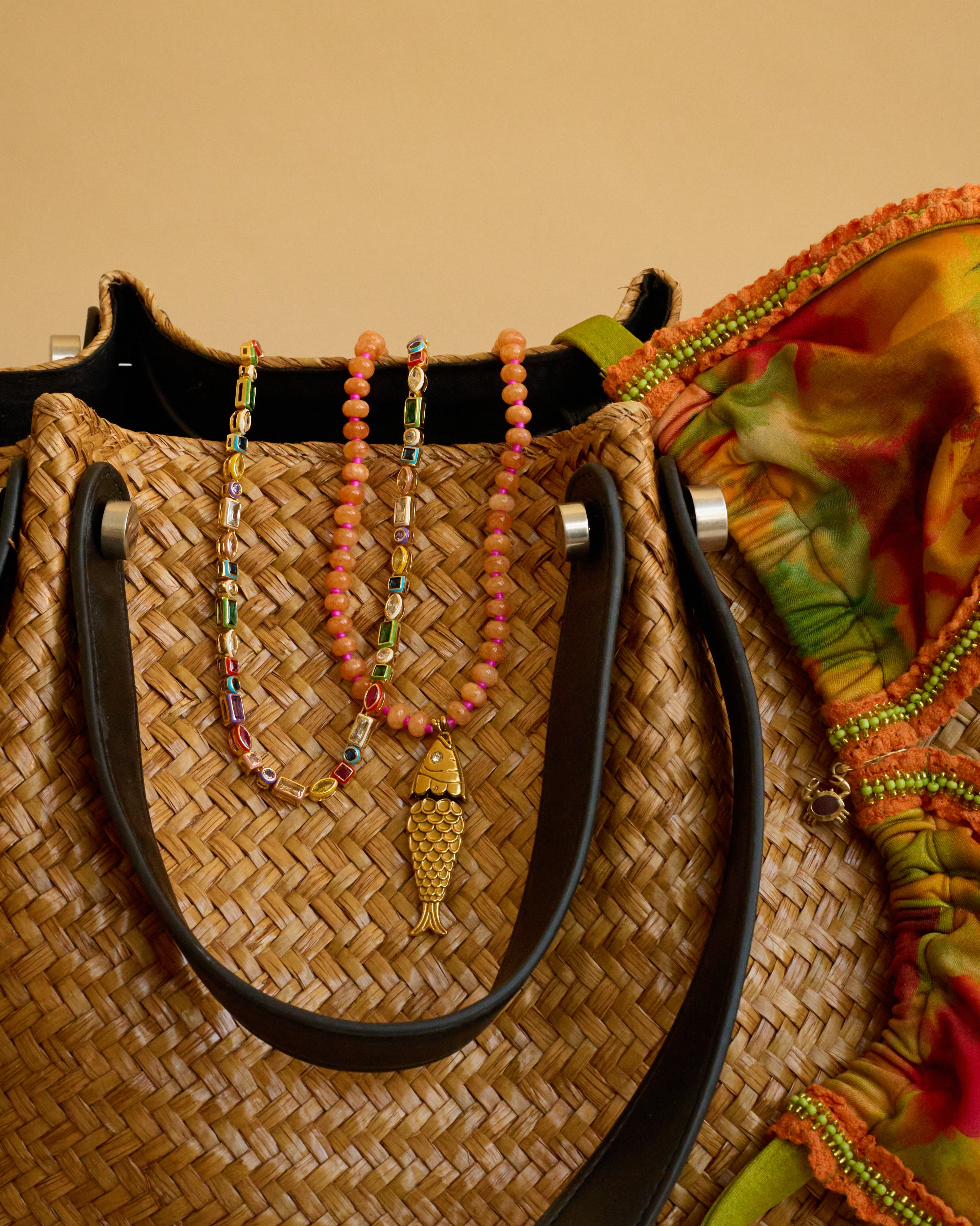 Woven handbag with colorful beads and a fish charm on a beige background