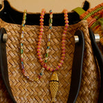 Woven bag with colorful beaded necklace and fish pendant on a beige background