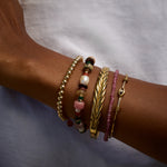 Close-up of a wrist wearing multiple gold and beaded bracelets on a neutral background