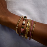 Close-up of a wrist wearing multiple gold and beaded bracelets on a neutral background