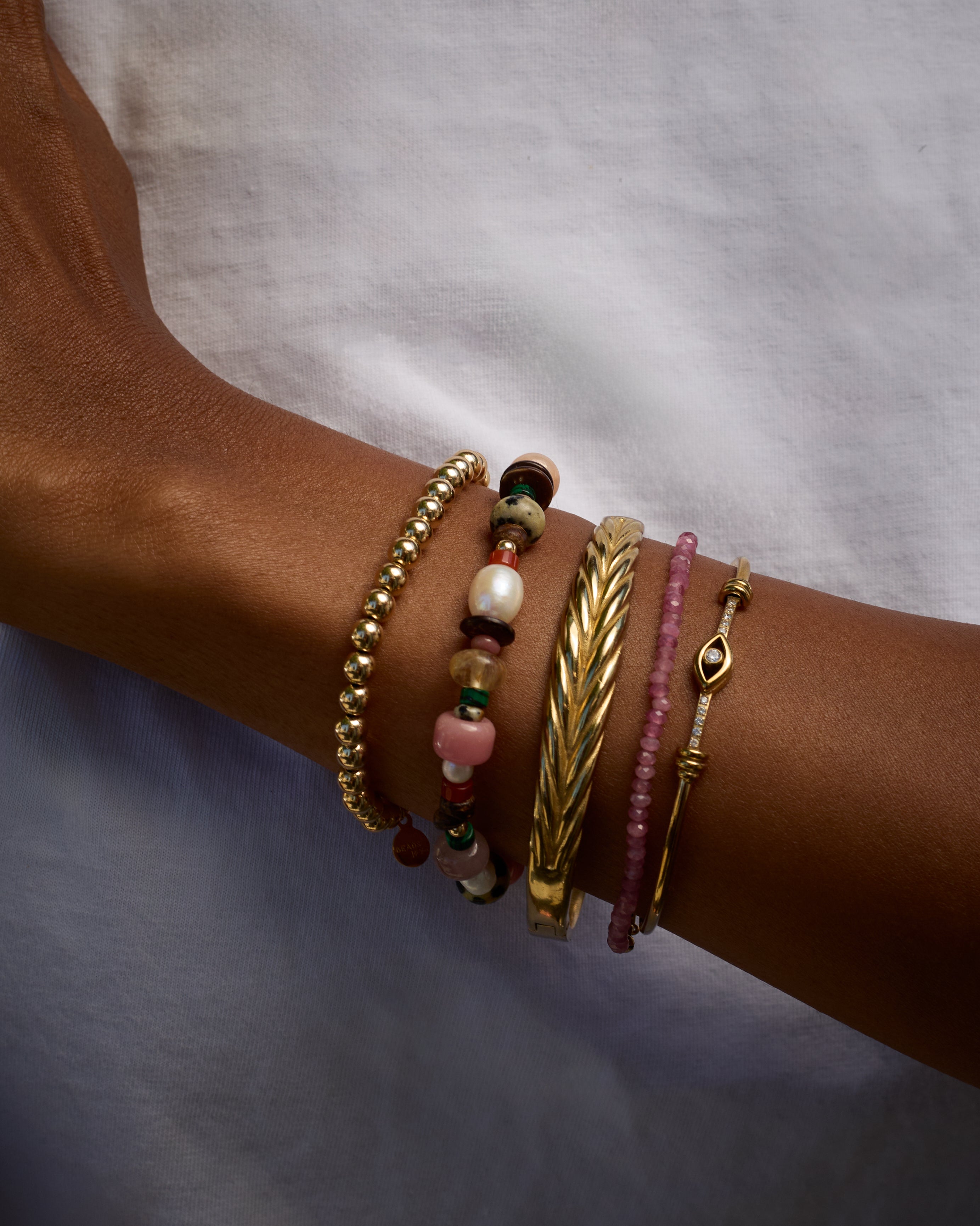 Close-up of a wrist wearing multiple gold and beaded bracelets on a neutral background