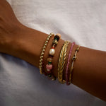 Close-up of a wrist wearing multiple bracelets on a neutral background