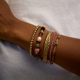 Close-up of a wrist wearing multiple bracelets on a neutral background