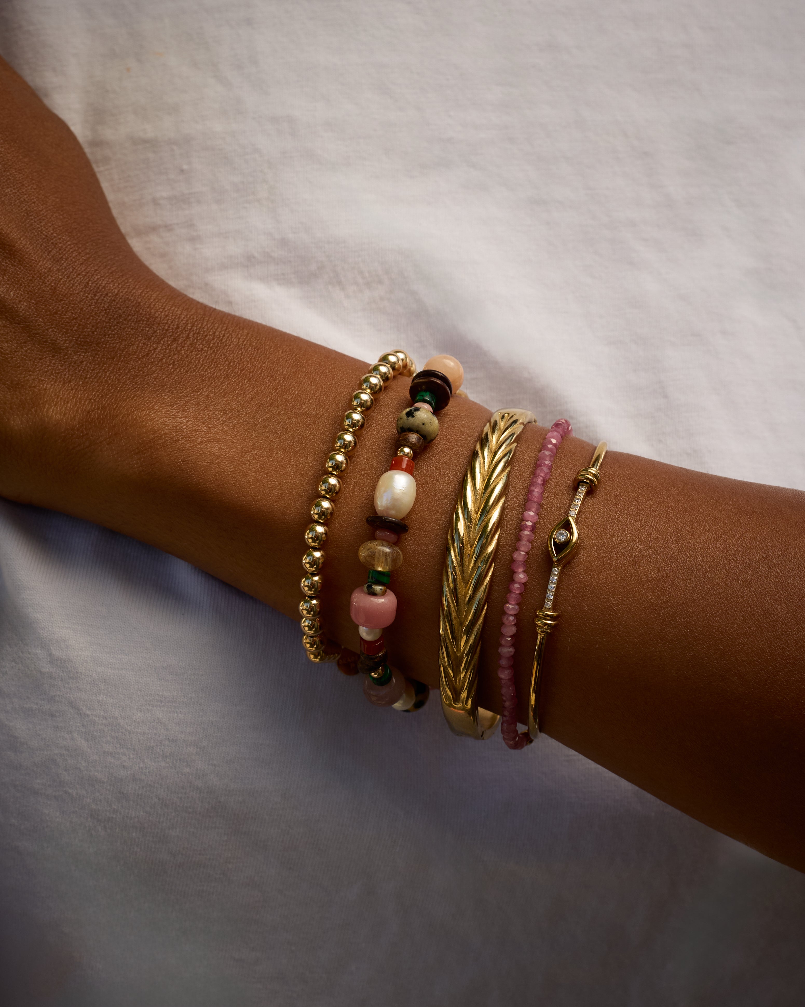 Close-up of a wrist wearing multiple bracelets on a neutral background