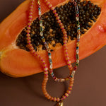 Beaded necklaces with a fish charm on a halved papaya.