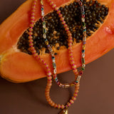 Beaded necklaces with a fish charm on a halved papaya.