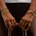 Close-up of hands wearing multiple bracelets and rings with a dark background