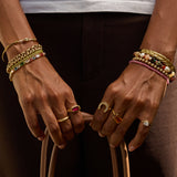 Close-up of hands wearing multiple bracelets and rings with a dark background