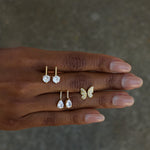 Hand wearing gold butterfly ring and earrings on a neutral background