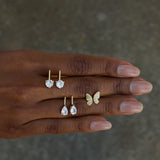 Hand wearing gold butterfly ring and earrings on a neutral background