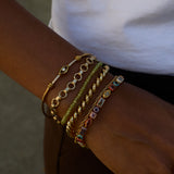 Close-up of a wrist wearing multiple gold and colorful bracelets on a blurred background