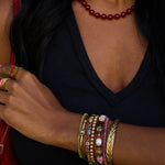 Close-up of a person's arm wearing multiple colorful bracelets and a ring, with a dark background.