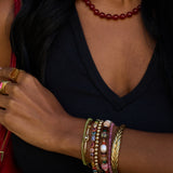 Close-up of a person's arm wearing multiple colorful bracelets and a ring, with a dark background.
