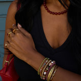 Person wearing multiple bracelets and rings with a red handbag and necklace.