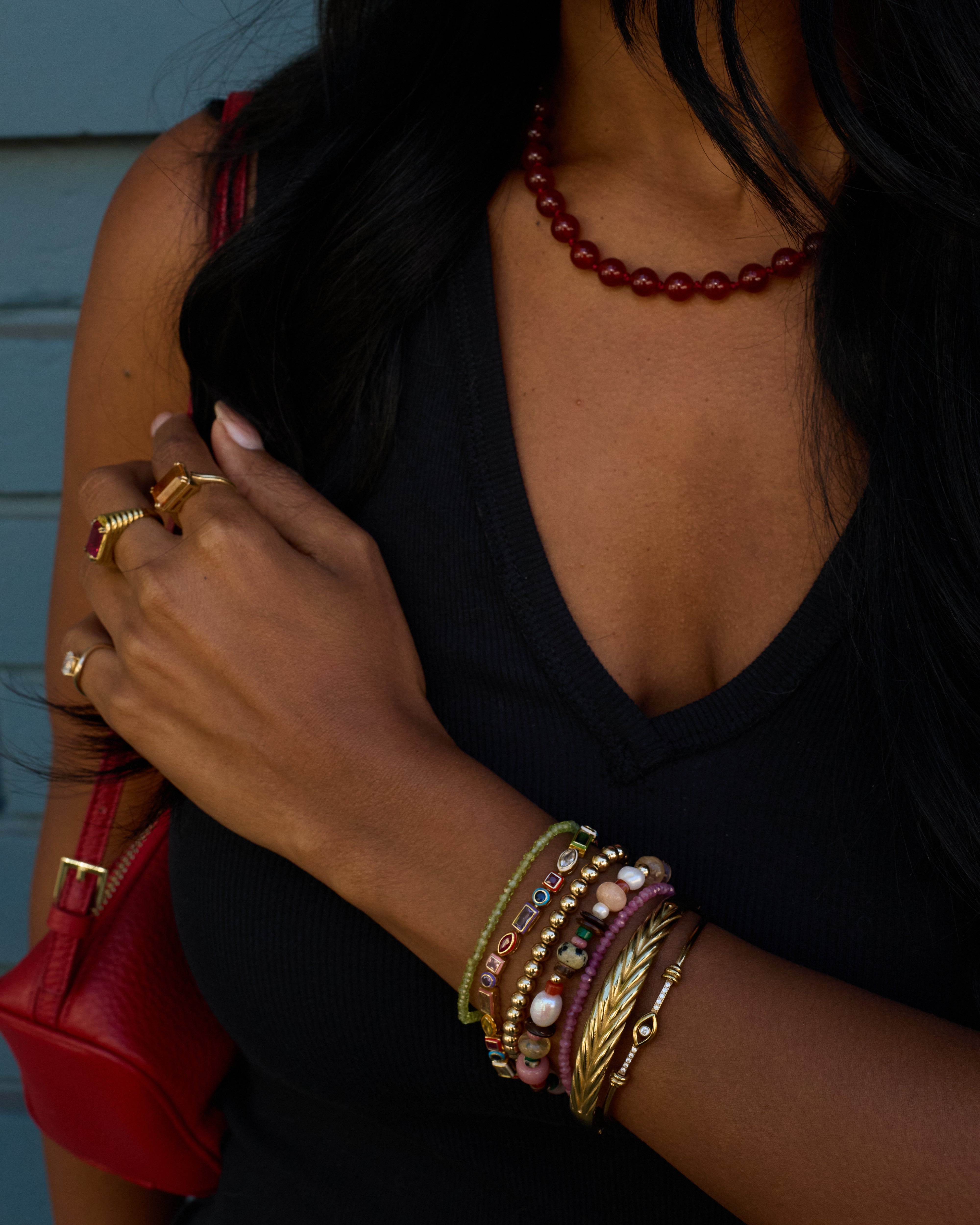 Person wearing multiple bracelets and rings with a red handbag and necklace.