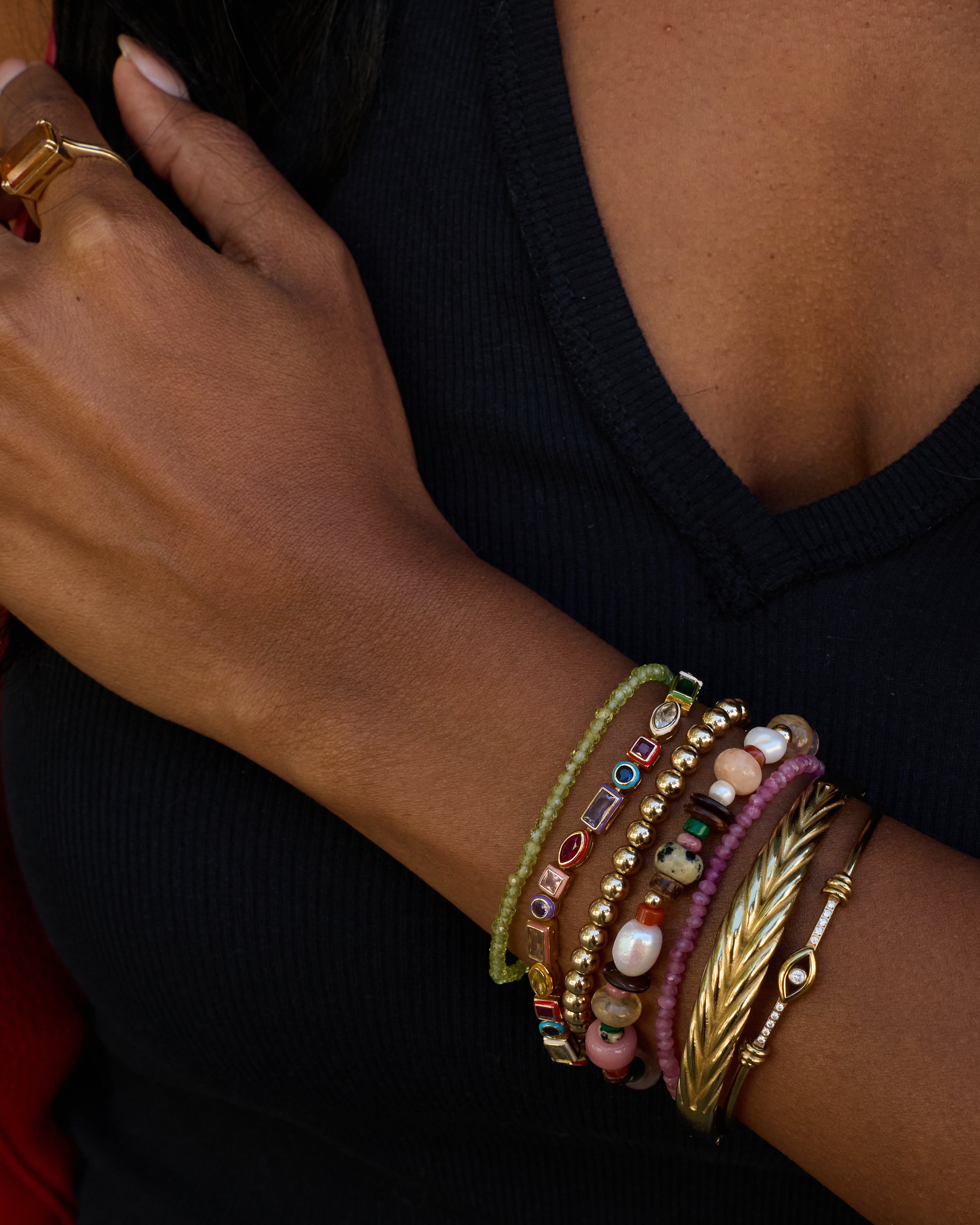 Close-up of a person's arm wearing multiple colorful bracelets on a black background