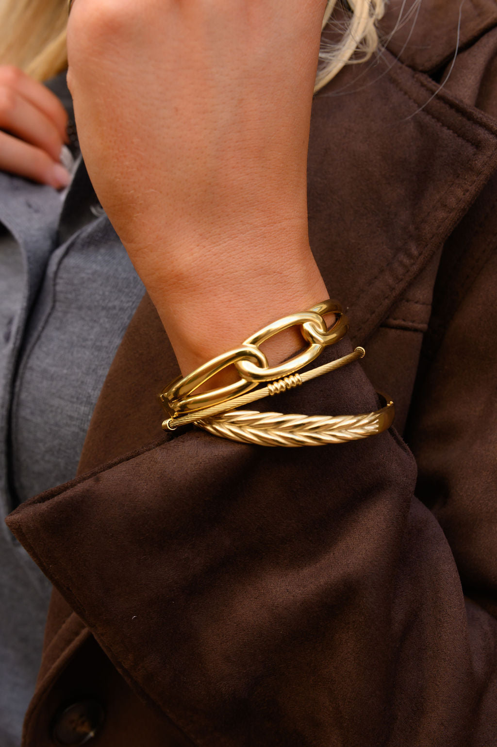 Close up of a person in a brown coat with gold bangles 