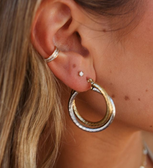 Close-up of an ear with multiple gold and silver earrings 