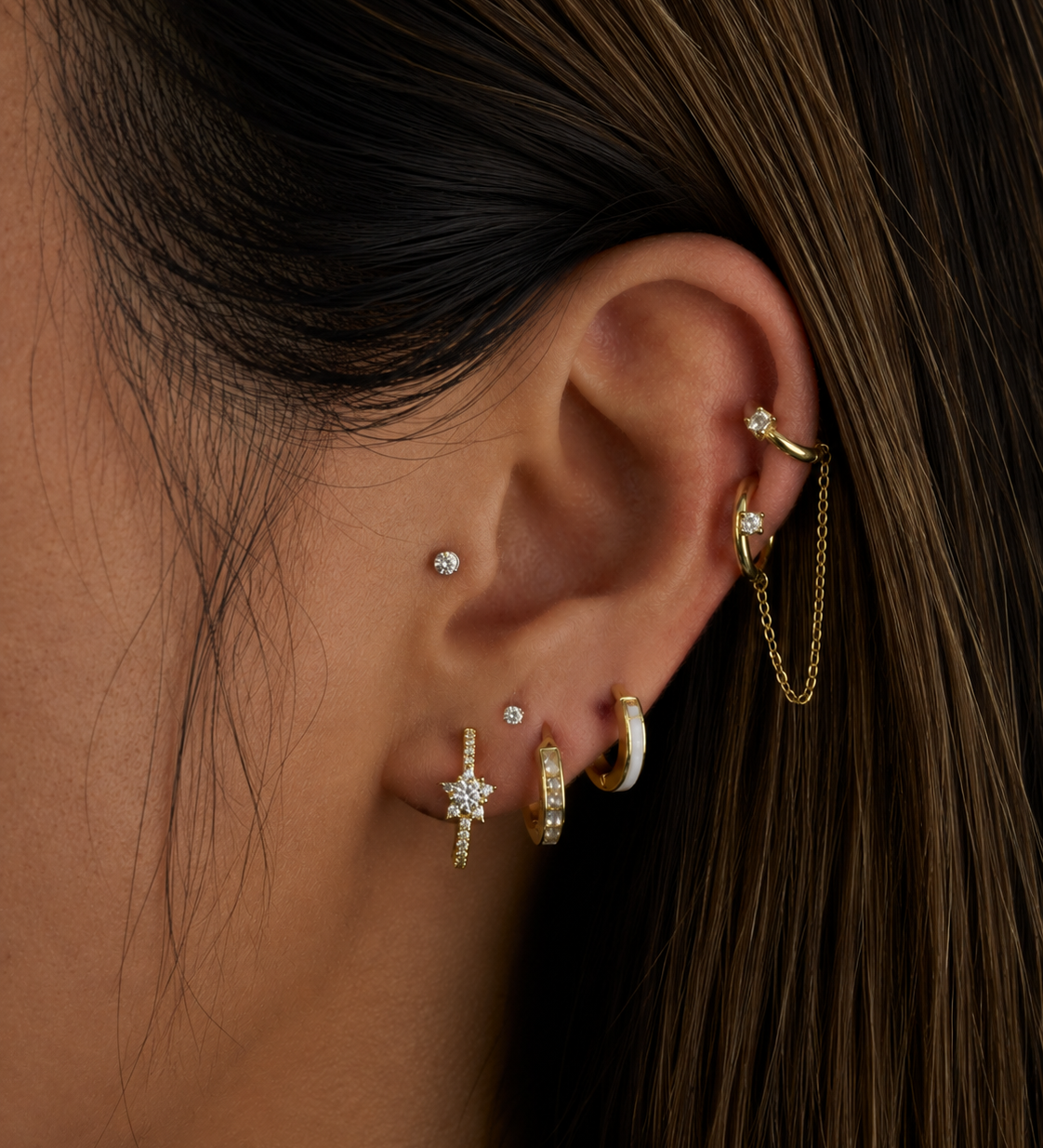 Close-up of an ear with multiple gold and diamond earrings against a dark background