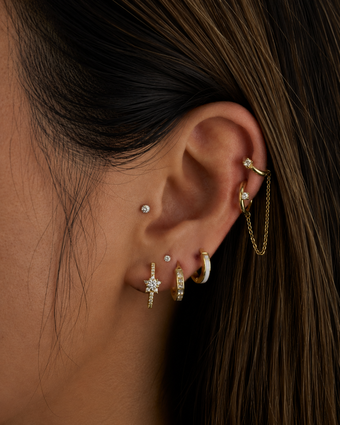 Close-up of an ear with multiple gold and diamond earrings against a dark background