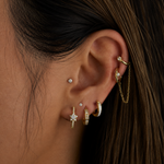 Close-up of an ear with multiple gold and diamond earrings against a dark background