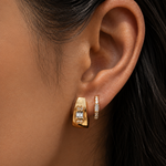Close-up of an ear wearing gold hoop earrings with clear gemstones.