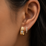 Close-up of an ear wearing gold hoop earrings with clear gemstones.