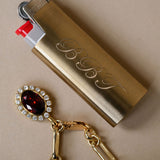 Gold lighter with 'BBJ' branding and a decorative keychain on a beige background