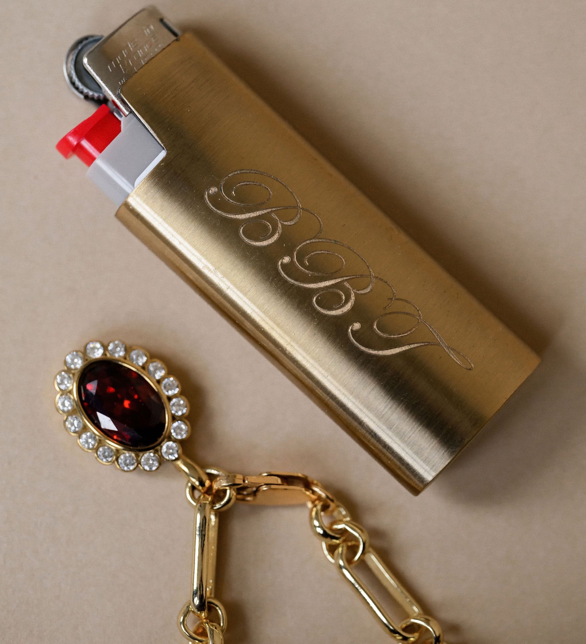 Gold lighter with 'BBJ' branding and a decorative keychain on a beige background