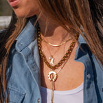 Close-up of a person wearing multiple gold necklaces with a denim jacket and white top.