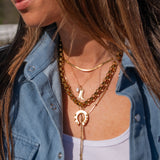 Close-up of a person wearing multiple gold necklaces with a denim jacket and white top.
