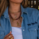 Woman wearing a blue denim jacket with horse designs, sunglasses, and layered necklaces.