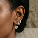 Close-up of an ear wearing gold heart-shaped earrings with a blurred background