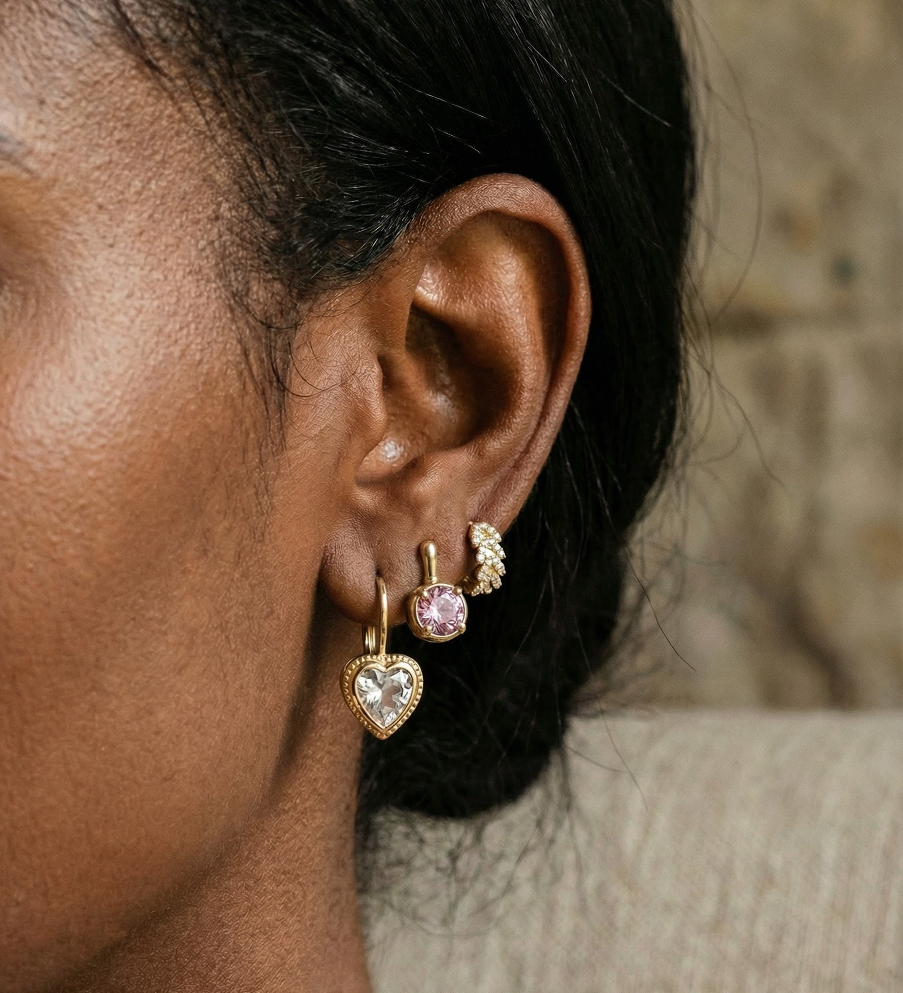 Close-up of an ear wearing gold heart-shaped earrings with a blurred background