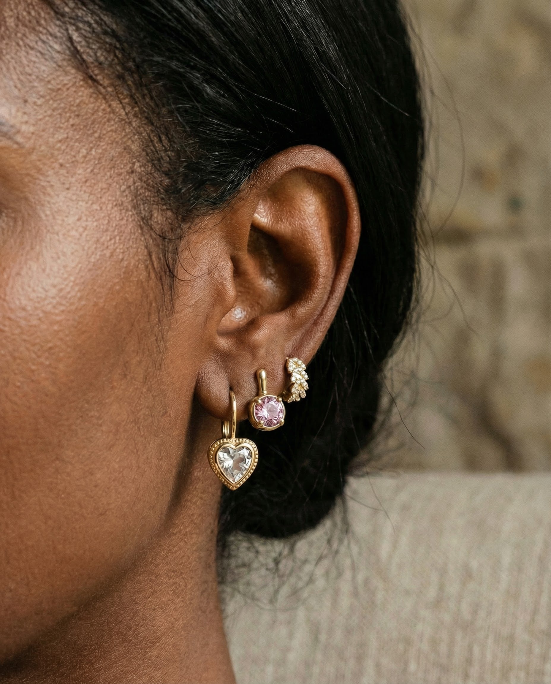 Close-up of an ear wearing gold heart-shaped earrings with a blurred background