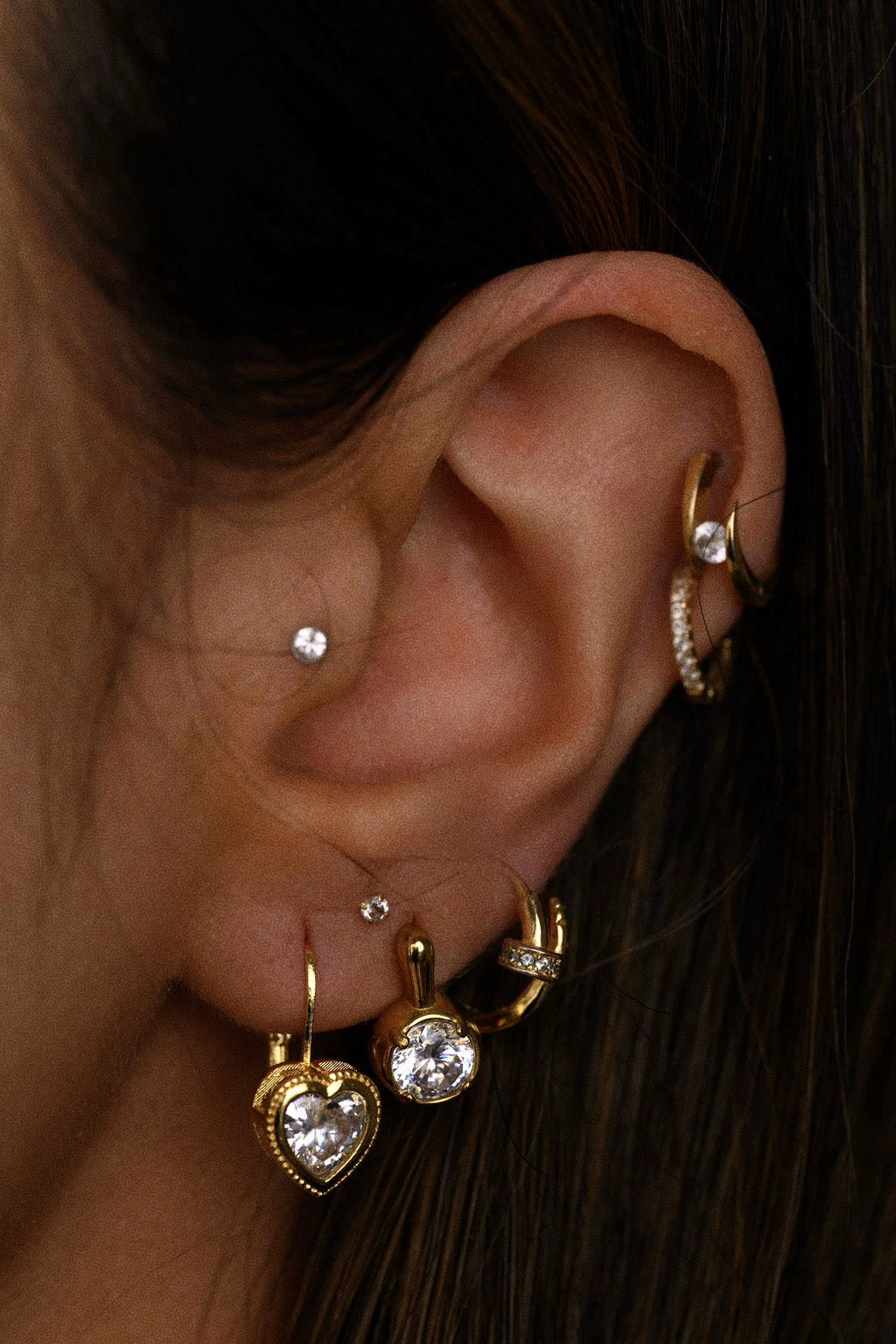 Close-up of an ear with multiple gold and crystal earrings 
